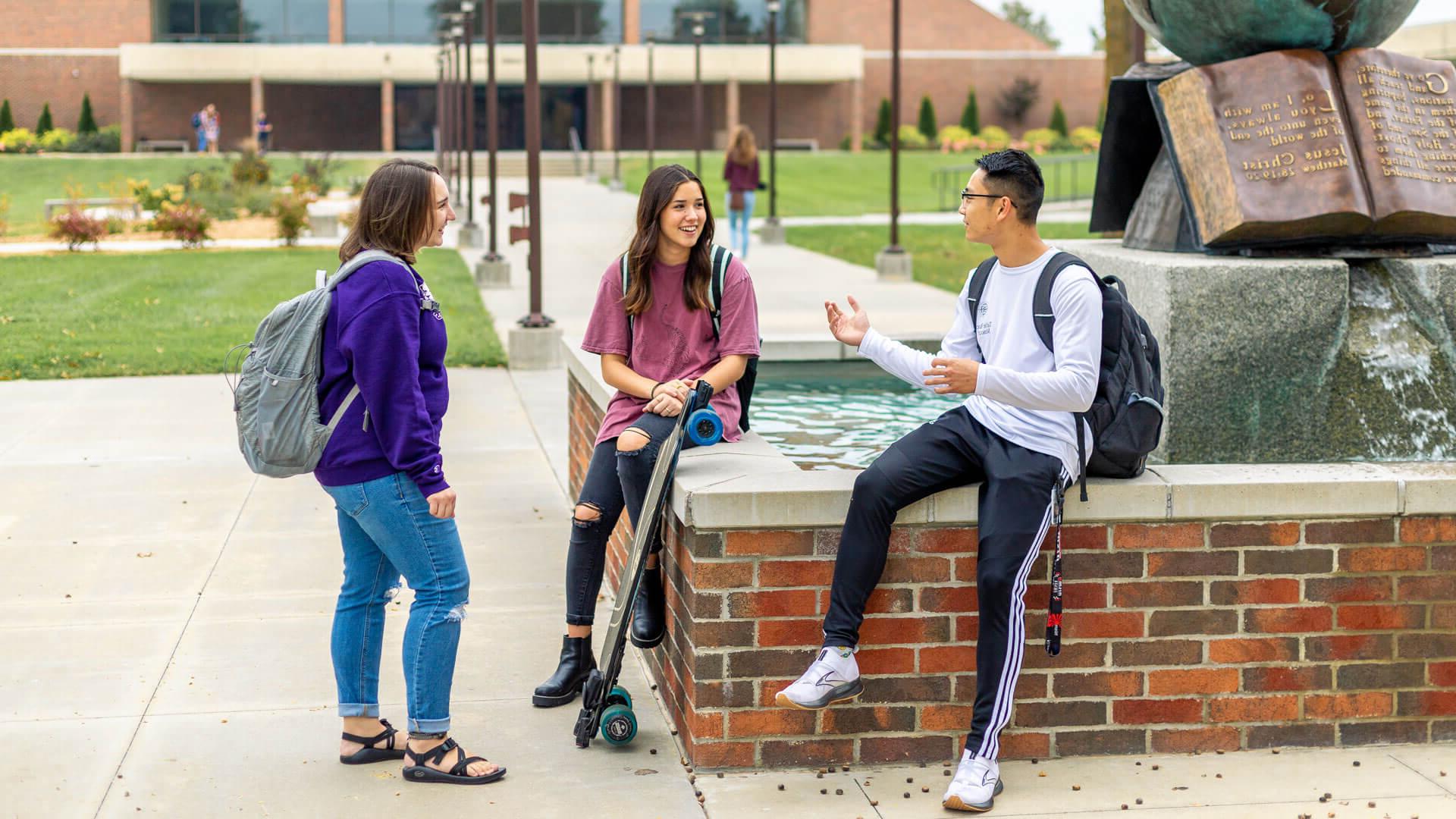 three students sitting and talking by globe water sculpture on campus forum